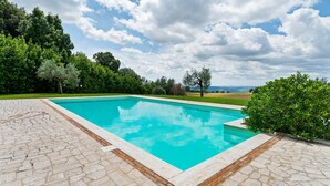 Une piscine rectangulaire à l’eau d’un bleu limpide, entourée d’une terrasse dallée dont le sol présente un motif en pierre.