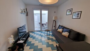 Een moderne woonkamer met een bank, een salontafel, een lamp en een eethoek die zichtbaar is door de glazen deuren.