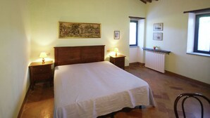 Een slaapkamer met een houten hoofdbord, een bed met een witte dekbedovertrek, twee bedlampen, een radiator en een raam met uitzicht.