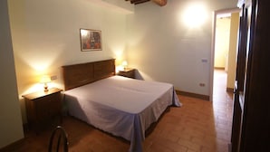 Un dormitorio con techo de madera, una cama con cubrecama blanco, dos mesitas de noche con lámparas y un cuadro en la pared.
