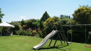 Un jardin avec un toboggan, des balançoires et un kiosque.