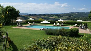 Un espace piscine agrémenté de chaises longues et de parasols, entouré de pelouses bien entretenues et offrant une vue panoramique sur des collines verdoyantes.