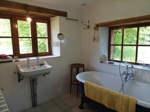 A bathroom with a bathtub, a sink, and a window with a view of greenery.