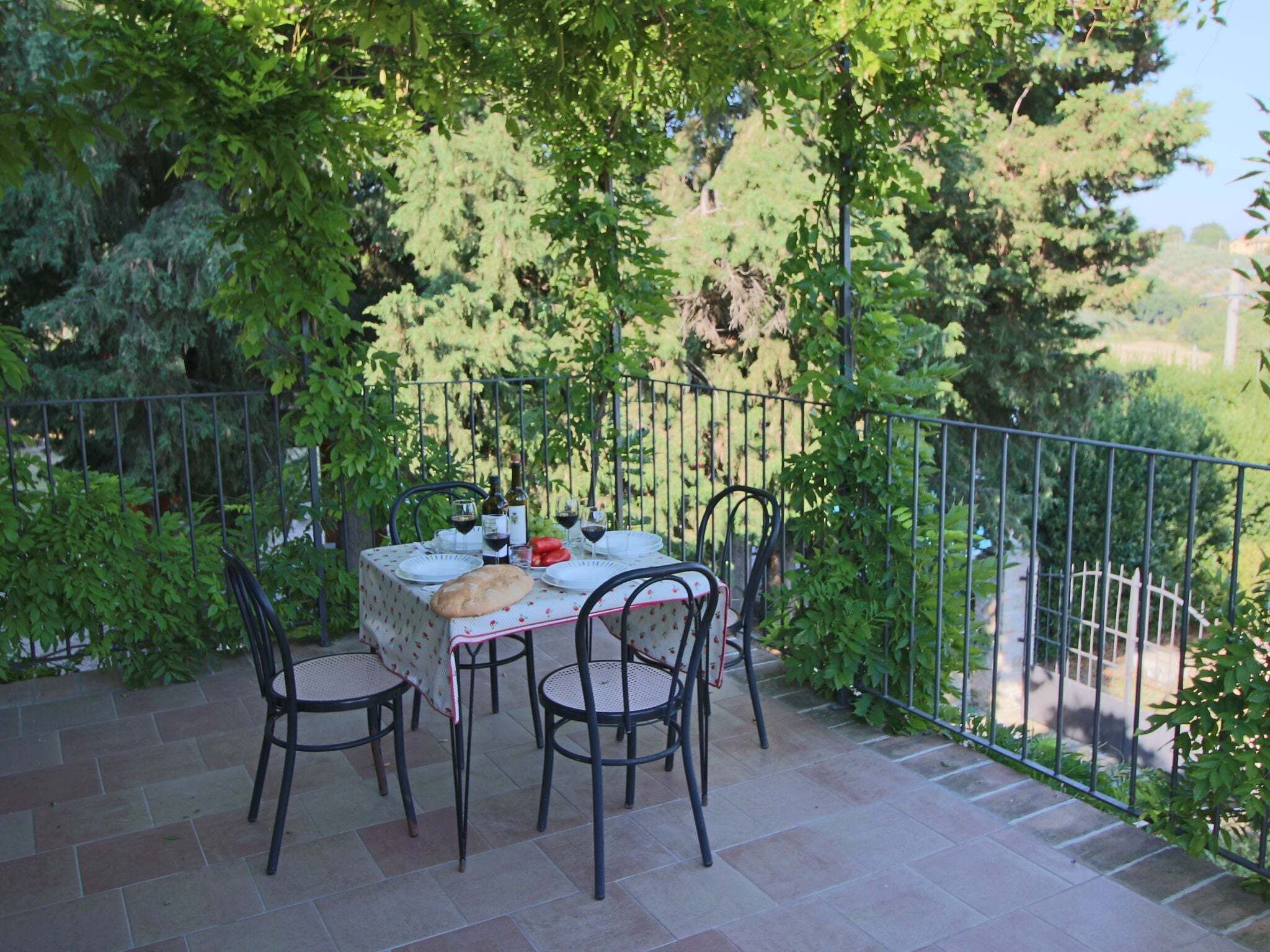 An outdoor patio with a table set for two, surrounded by chairs, and a railing.