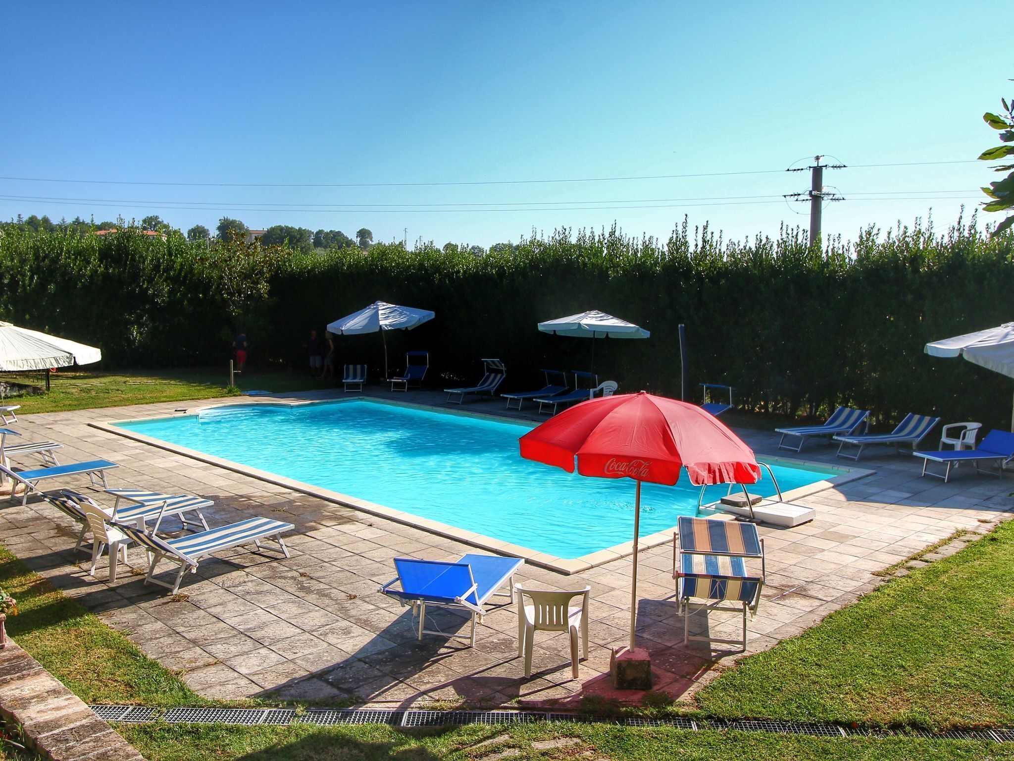 A rectangular swimming pool with a tiled deck, surrounded by lounge chairs and umbrellas.