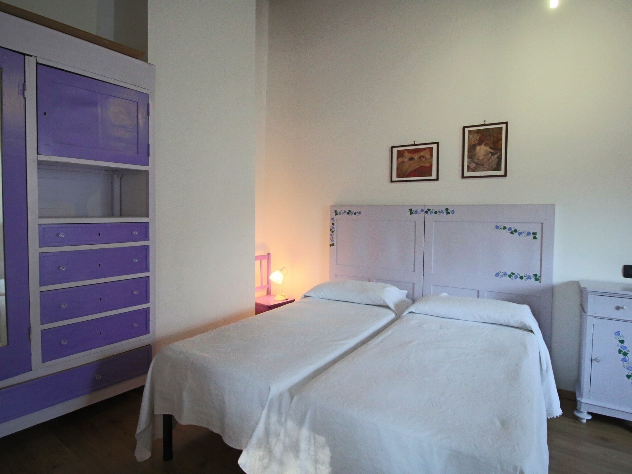A bedroom with two beds, a purple wardrobe, and two framed pictures on the wall.