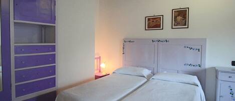 A bedroom with two beds, a purple wardrobe, and two framed pictures on the wall.