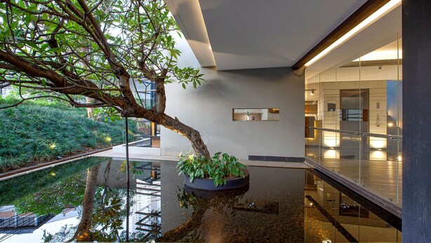 Espaço moderno em ambientes internos com uma fonte refletora, um jardim vertical e guarda-corpo de vidro com vista para um nível inferior.