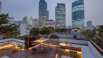 Eine Dachterrasse mit Holztischen und -stühlen, einer Sitzgelegenheit und einer Skyline im Hintergrund.
