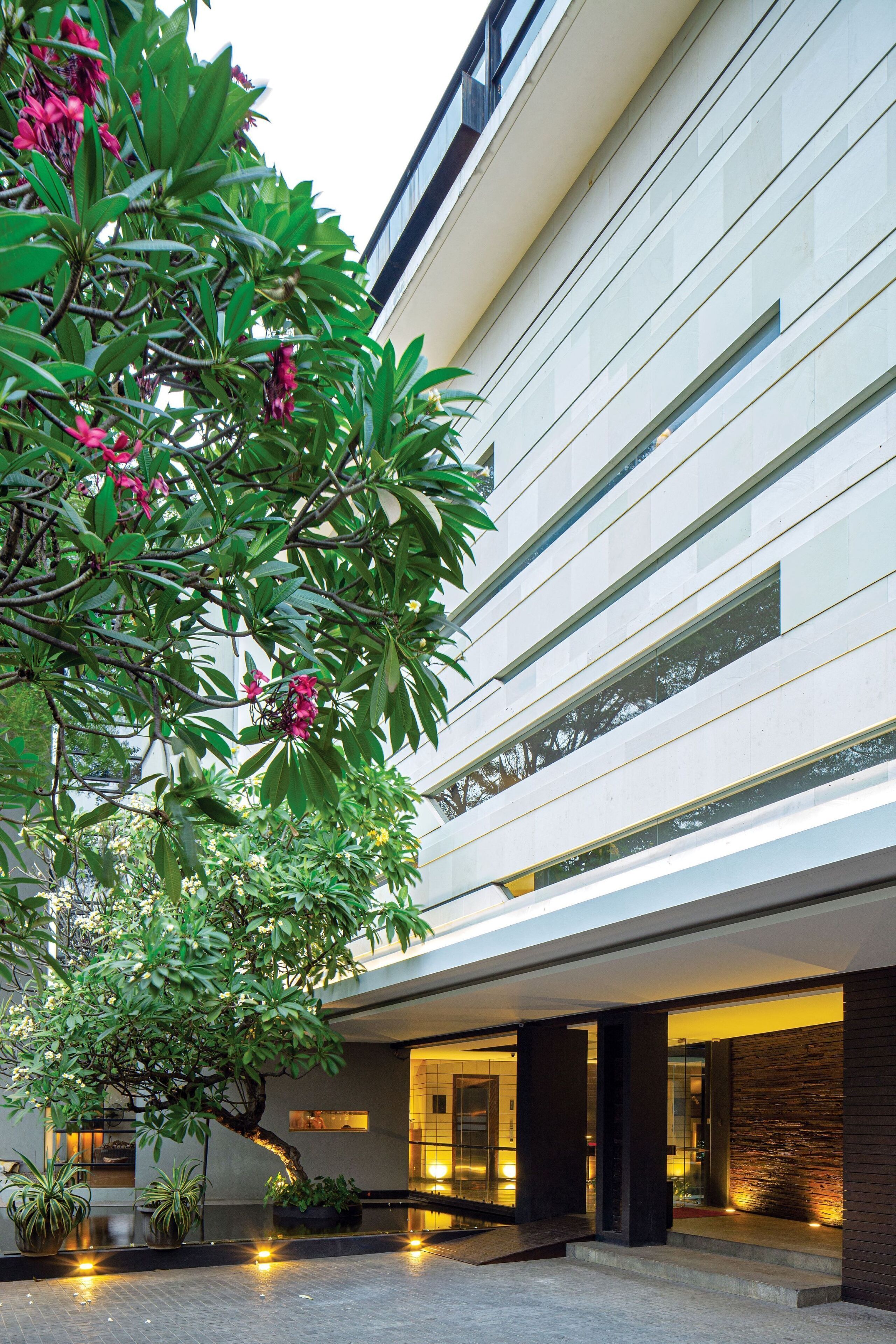 A modern building with a glass facade, a courtyard with potted plants, and a well-lit entrance.