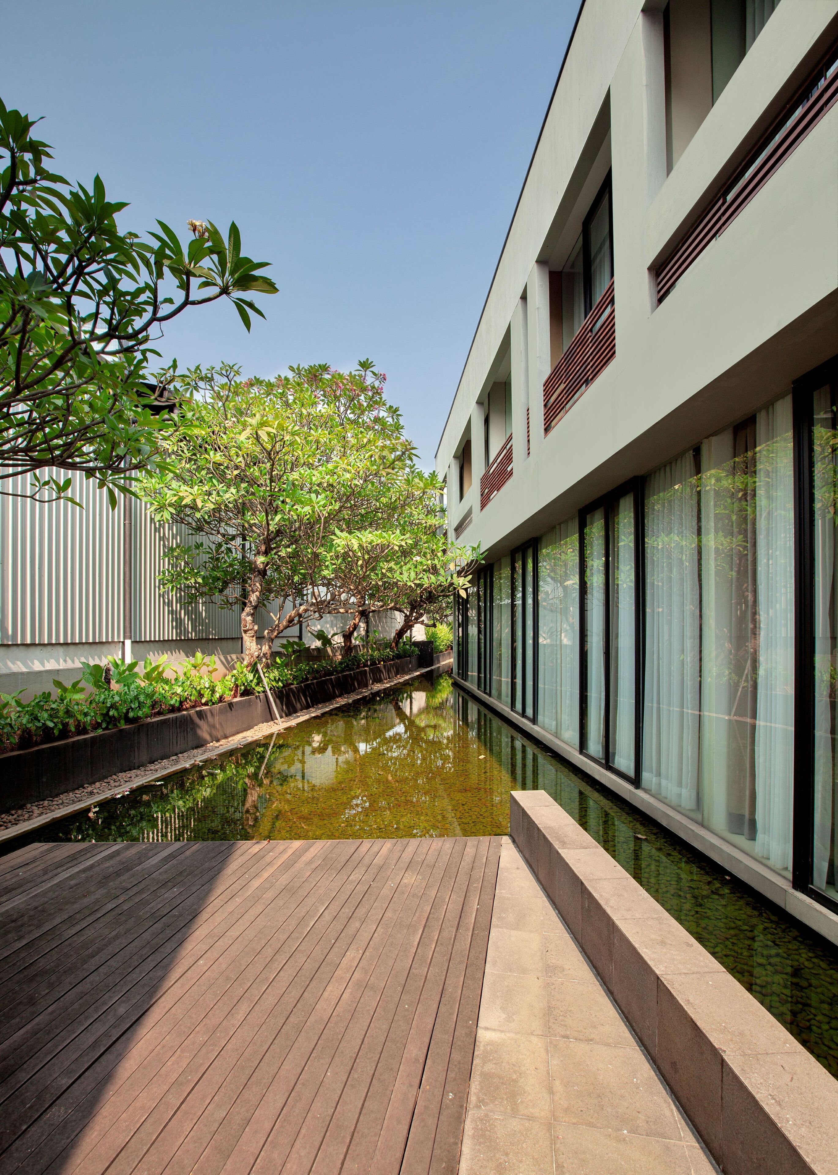 A modern building with large windows, a wooden deck, and a narrow water channel.