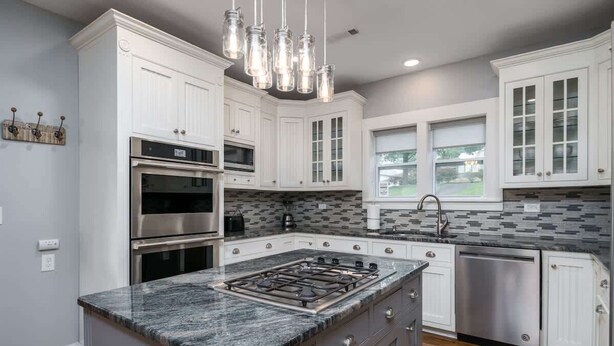 A modern kitchen with white cabinetry, a granite countertop, stainless steel appliances, and a hanging light fixture. - Downtown Walk Around (Blue Ridge)