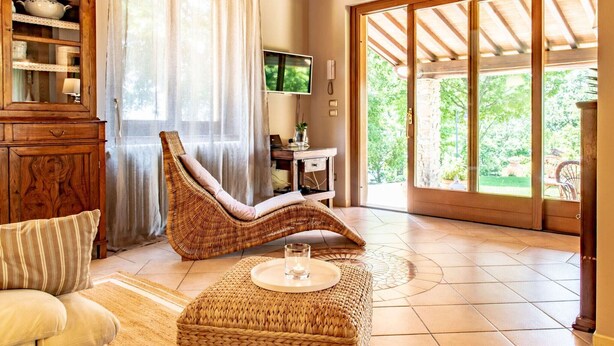 A cozy living room with a wicker chair, a sofa, a wooden cabinet, and a television. - Holiday Home in Tuscany with Pool & Olive Trees (Montecatini Terme)