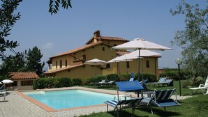 A pool area with lounge chairs and umbrellas, surrounded by a building with a tiled roof.