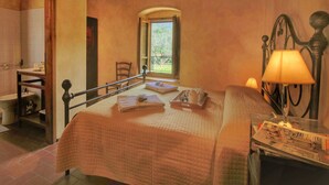 A bedroom with a bed, a window, a bedside table with a lamp, and a view of the outdoors.