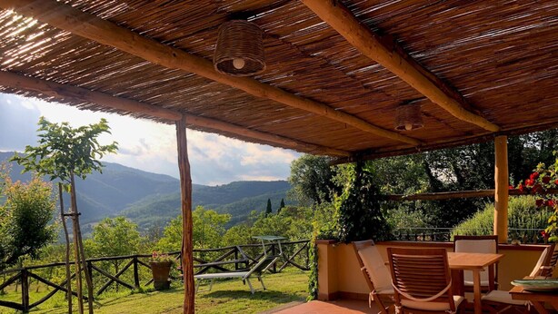 A covered patio with a table and chairs, overlooking a lush garden and mountains. - Scenic Stay in Restored Retreat (Arezzo)