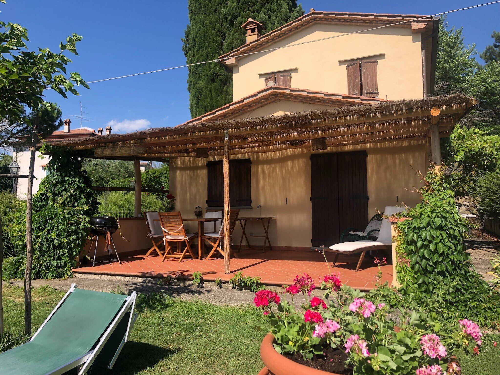 Une maison dotée d’un patio couvert, d’un coin repas et d’un jardin fleuri.