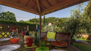 Ein Holz-Esstisch im Freien, gedeckt für eine Mahlzeit, mit freiem Blick auf den umliegenden Garten und einem Haus im Hintergrund.