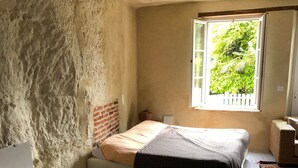 A bedroom with a bed, a window, a brick wall, and a tiled floor. - Troglodyte (Nazelles-Négron)