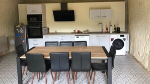 A compact kitchen with a dining area, including a table and chairs, a built-in oven, a microwave, a washing machine, and a flat-screen TV. - Troglodyte (Nazelles-Négron)