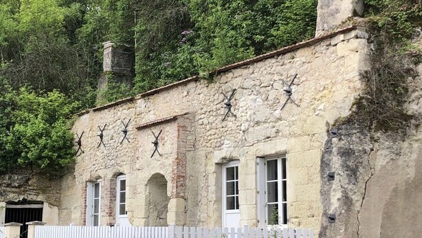 A rustic stone building with multiple windows, a white picket fence, and a chimney. - Troglodyte (Nazelles-Négron)