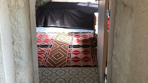 A narrow doorway leading to a room with a bed, patterned rug, and a brick wall. - Troglodyte (Nazelles-Négron)