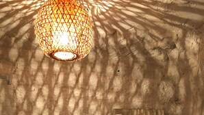 A bathroom with a textured wall, a white sink, a mirror, and a hanging light fixture casting shadows. - Troglodyte (Nazelles-Négron)