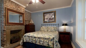 Un dormitorio con chimenea de ladrillo, una cama con cubrecama floral, ventilador de techo y un cuadro en la pared.