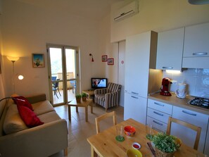 A compact living space with a sofa, a dining table, a kitchen area, and a balcony.