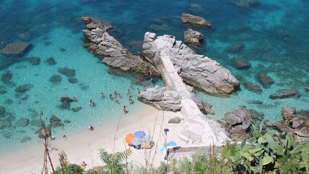 Een strand met helder turquoise water, rotsformaties en mensen die zwemmen.