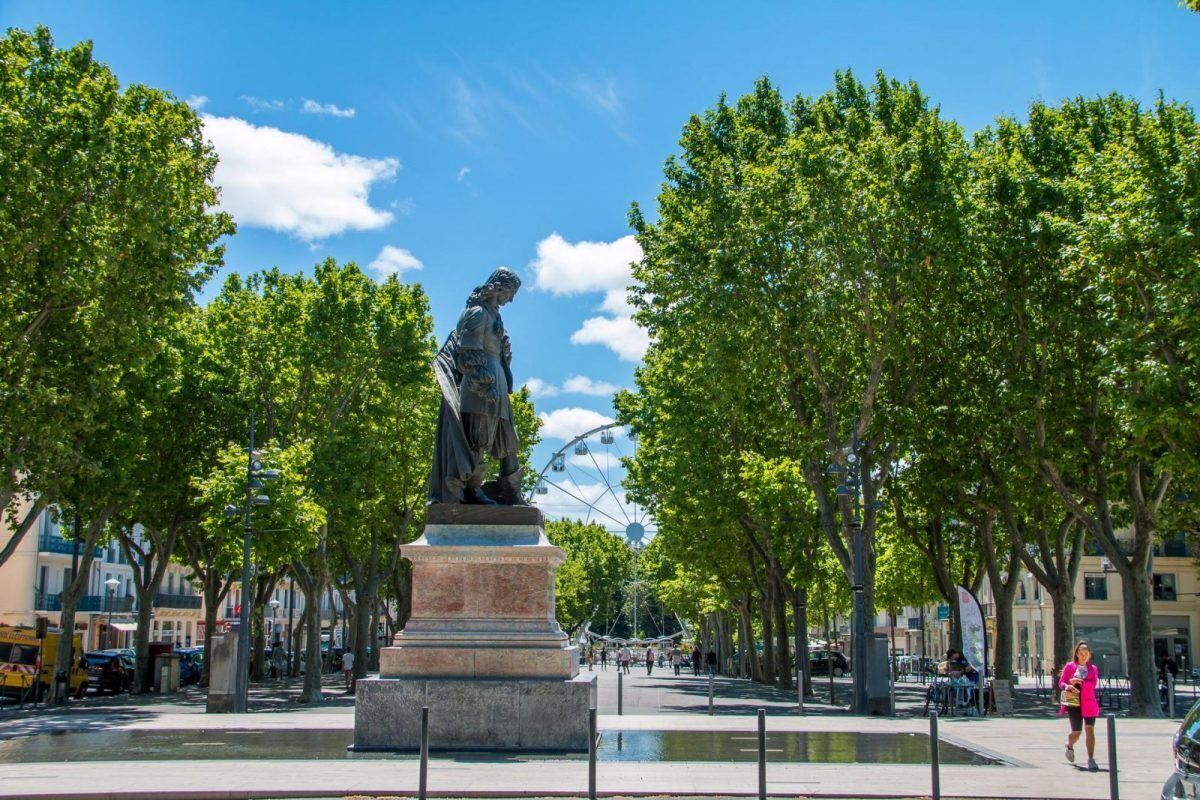 A statue in a public square with trees and a Ferris wheel in the background.