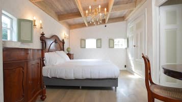 A bedroom with a wooden ceiling, a bed, a dresser, a chandelier, and a window with shutters.