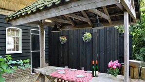 Puinen pergola, jonka päällä on ruutukuviollinen pöytäliina, kaksi viinipulloa ja maljakko täynnä kukkia.