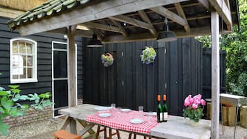 A wooden pergola with a checkered tablecloth, two wine bottles, and a vase of flowers.