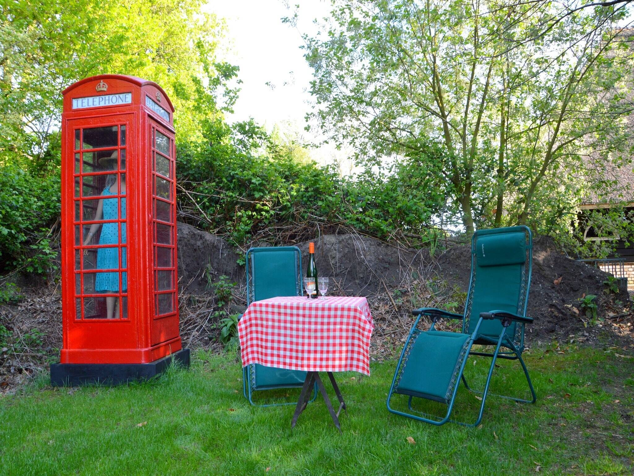 A red telephone booth with a table and two chairs in a grassy area.