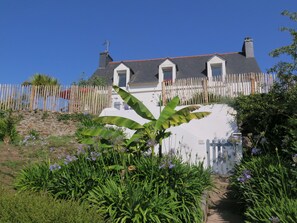 Una casa con un muro de piedra, una cerca de madera y un jardín con diversas plantas y flores.