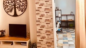 Uma sala de estar com uma TV sobre um suporte de madeira, arte de parede com tema de árvore decorativa, parede com padrão de tijolos e chão quadriculado.