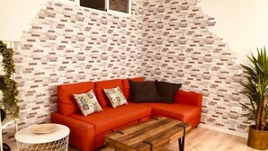 Uma sala de estar com um sofá seccional vermelho, uma mesa de centro de madeira e uma parede com padrão de tijolos.