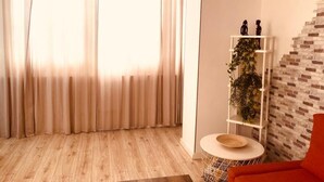 Uma sala de estar moderna com uma janela grande, um sofá vermelho, uma mesa redonda branca e uma parede com padrão de tijolos.