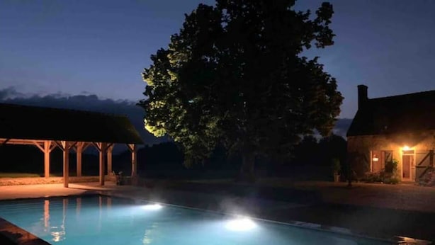 A nighttime swimming pool with a covered pavilion and a house in the background.