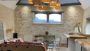 A rustic room with a stone wall, a foosball table, a fireplace, and a window with a view.