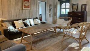 A rustic room with a wooden ceiling, a sofa with cushions, a wicker table, and a dresser.