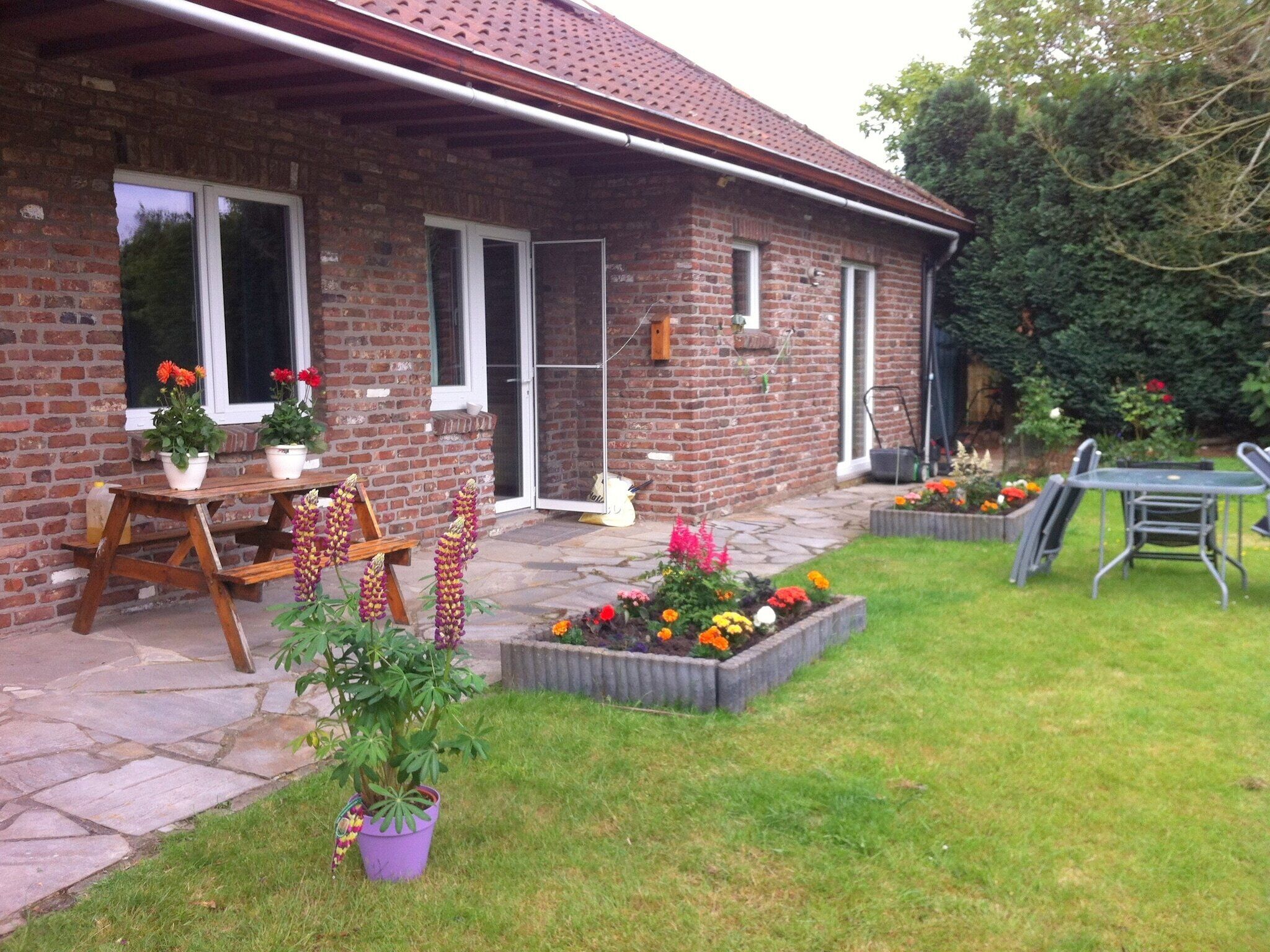 Une maison en briques avec un patio, une table en bois et des plantes en pot.