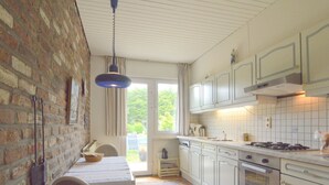 Cucina con mobili bianchi, piano cottura a gas e parete in mattoni.