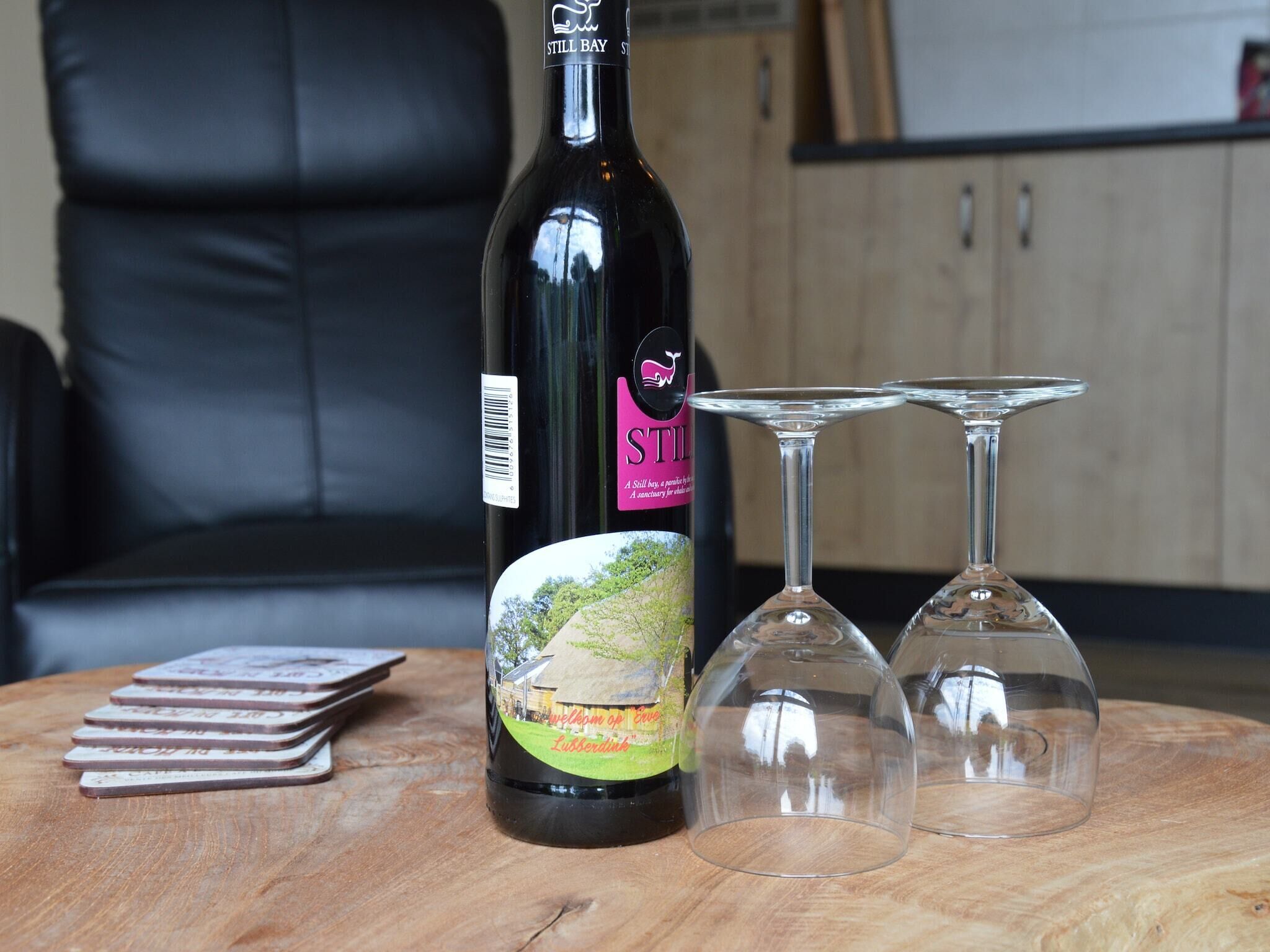 Una botella de vino Still Bay, dos copas de vino y una baraja de cartas sobre una mesa de madera.