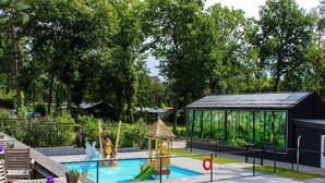 Una piscina con tobogán, zona de juegos y terraza de madera con sillas.