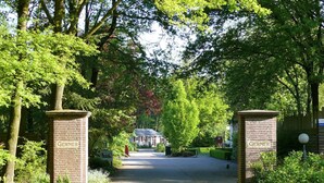 A pathway leading to a building with 'Gerner' signs on either side, surrounded by lush greenery. - Tranquil Forest Retreat (Dalfsen)