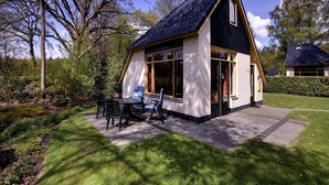 A small, single-story house with a sloped roof, large windows, and a patio with outdoor furniture. - Tranquil Forest Retreat (Dalfsen)