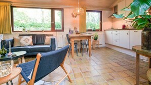 A cozy living area with a sofa, a dining table, and a kitchen area with cabinets and a plant. - Holiday Home in Zorgvlied near Drents (Zorgvlied)