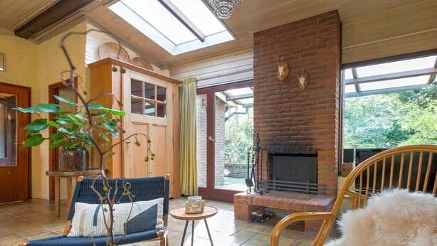 A cozy room with a fireplace, wooden furniture, and a view of greenery outside. - Holiday Home in Zorgvlied near Drents (Zorgvlied)